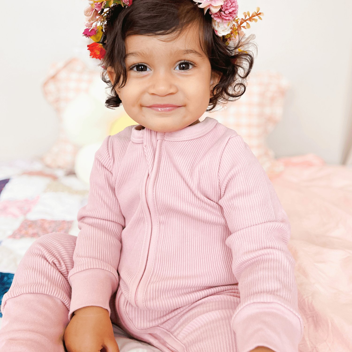 Toddler sat smiling wearing the Blush Ribbed Sleepsuit made from bamboo and organic cotton from GrowGrows