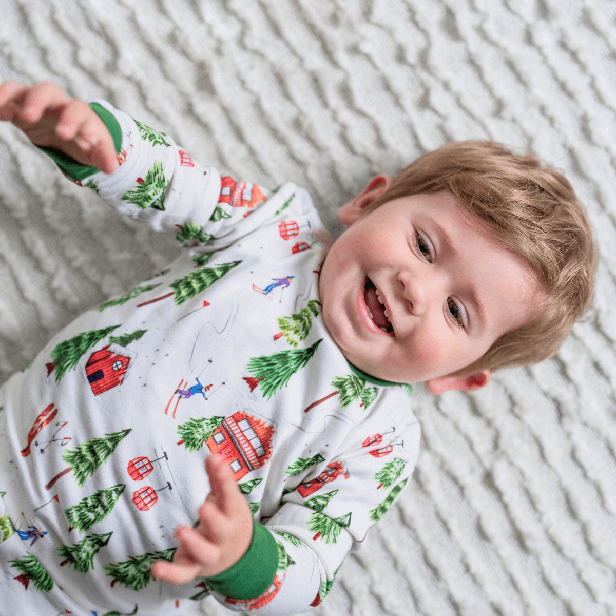 Toddler lying on the floor wearing the Alpine Adventures Pyjamas with chalet, fir tree and skier print and forest green trim made from bamboo and organic cotton from GrowGrows