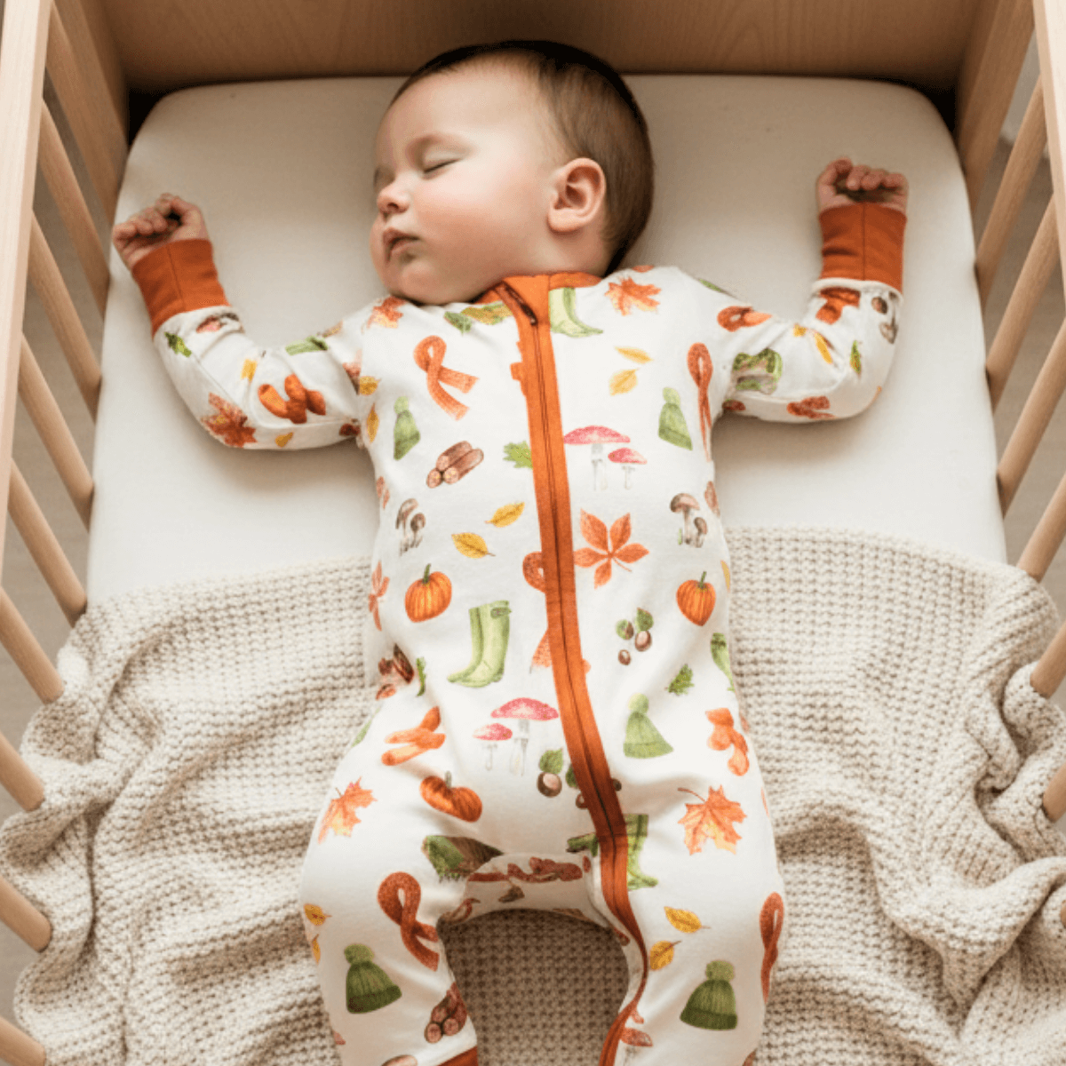 Baby lying asleep in the cot wearing the Autumnal Amazes Sleepsuit with pumpkin and autumn print made from bamboo and organic cotton from GrowGrows