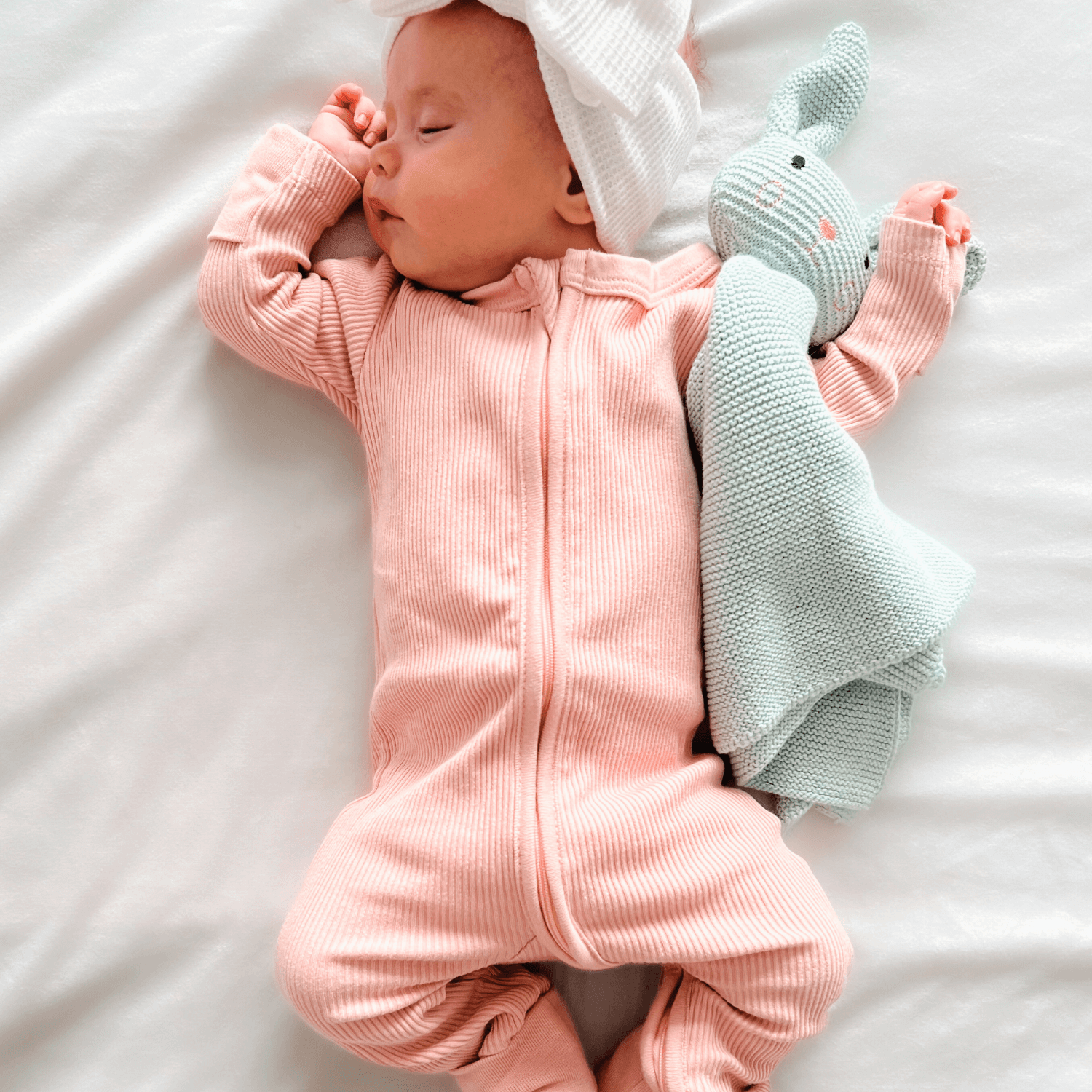 Baby asleep wearing the Blush Ribbed Sleepsuit made from bamboo and organic cotton from GrowGrows and holding the Bunny Comforter