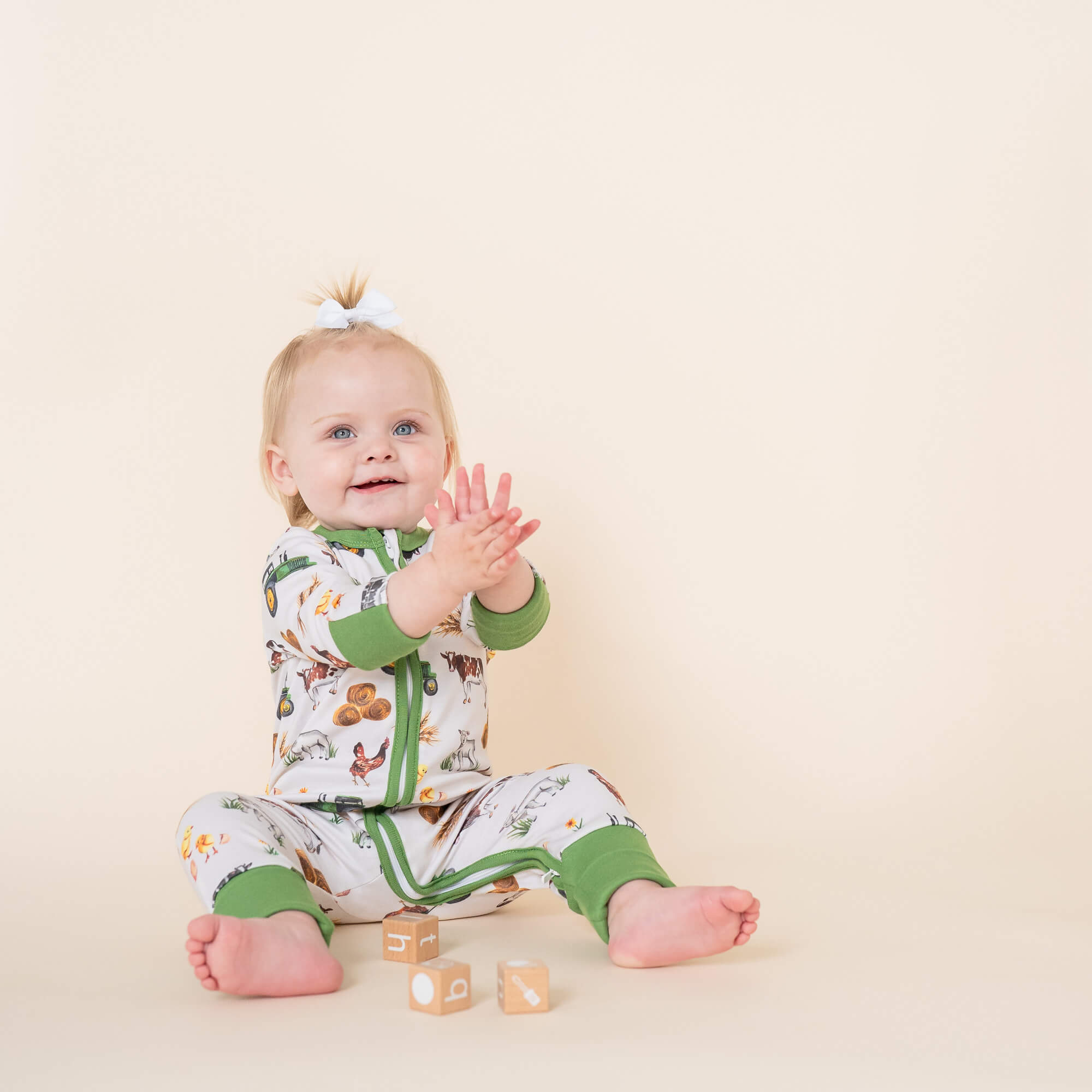 Baby sat clapping hands wearing the Family Farm Sleepsuit with farm print made from bamboo and organic cotton from GrowGrows