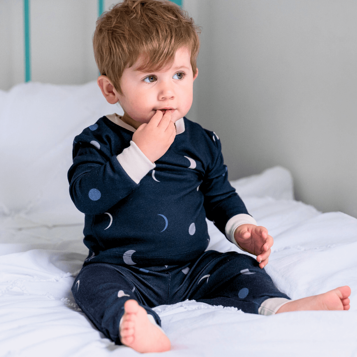 Toddler sat in bed wearing the Midnight Moons Pyjamas with navy moon phase print made from bamboo and organic cotton from GrowGrows