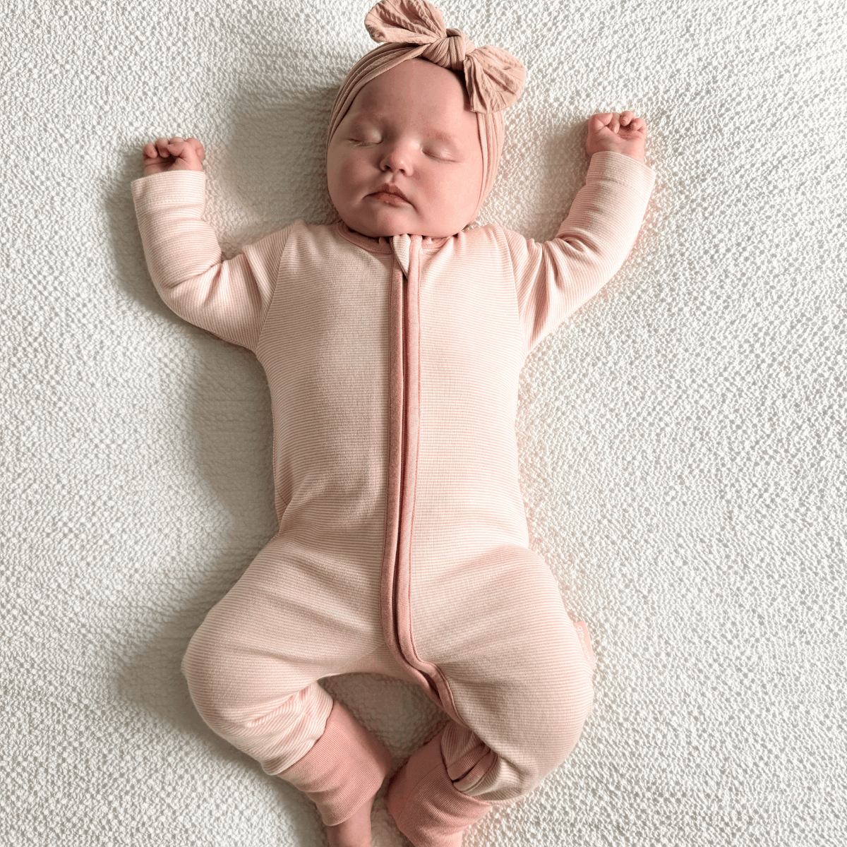 Newborn baby lying down in a Pink Pinstripe Sleepsuit with classic pink stripe design made from bamboo and organic cotton from GrowGrows