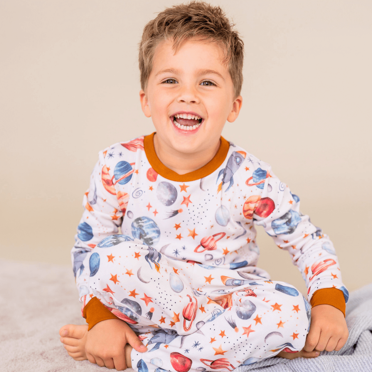 Child sat smiling wearing the Plentiful Planets Pyjamas with planet and space print made from bamboo and organic cotton from GrowGrows