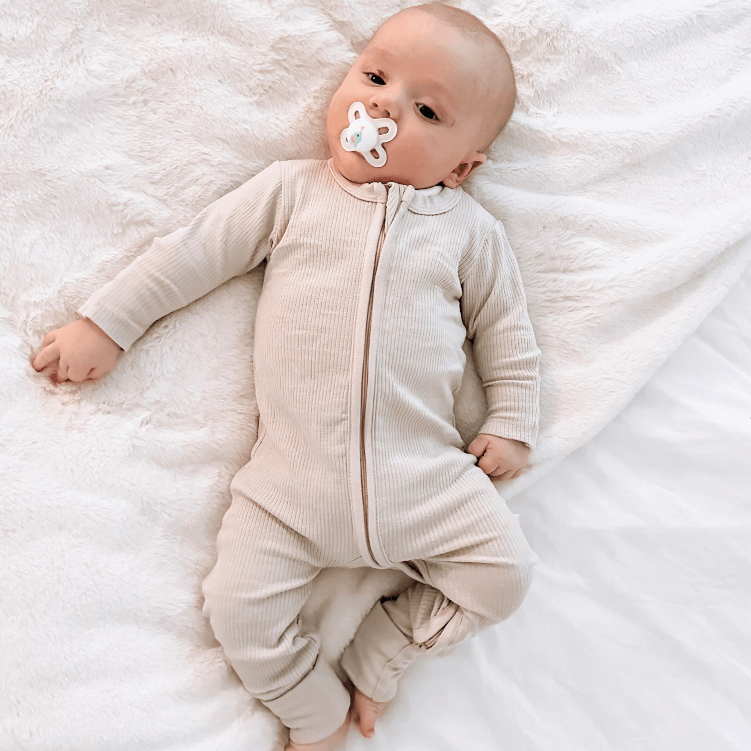 Baby lying on a soft white blanket wearing the Cashmere Ribbed Sleepsuit made from bamboo and organic cotton from GrowGrows