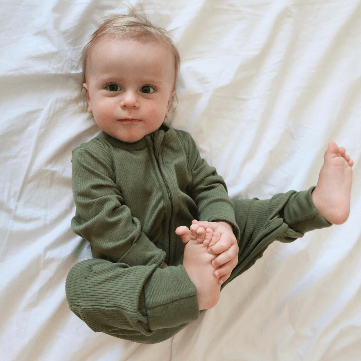 Baby playing with their toes wearing the GrowGrows Forest Ribbed Sleepsuit
