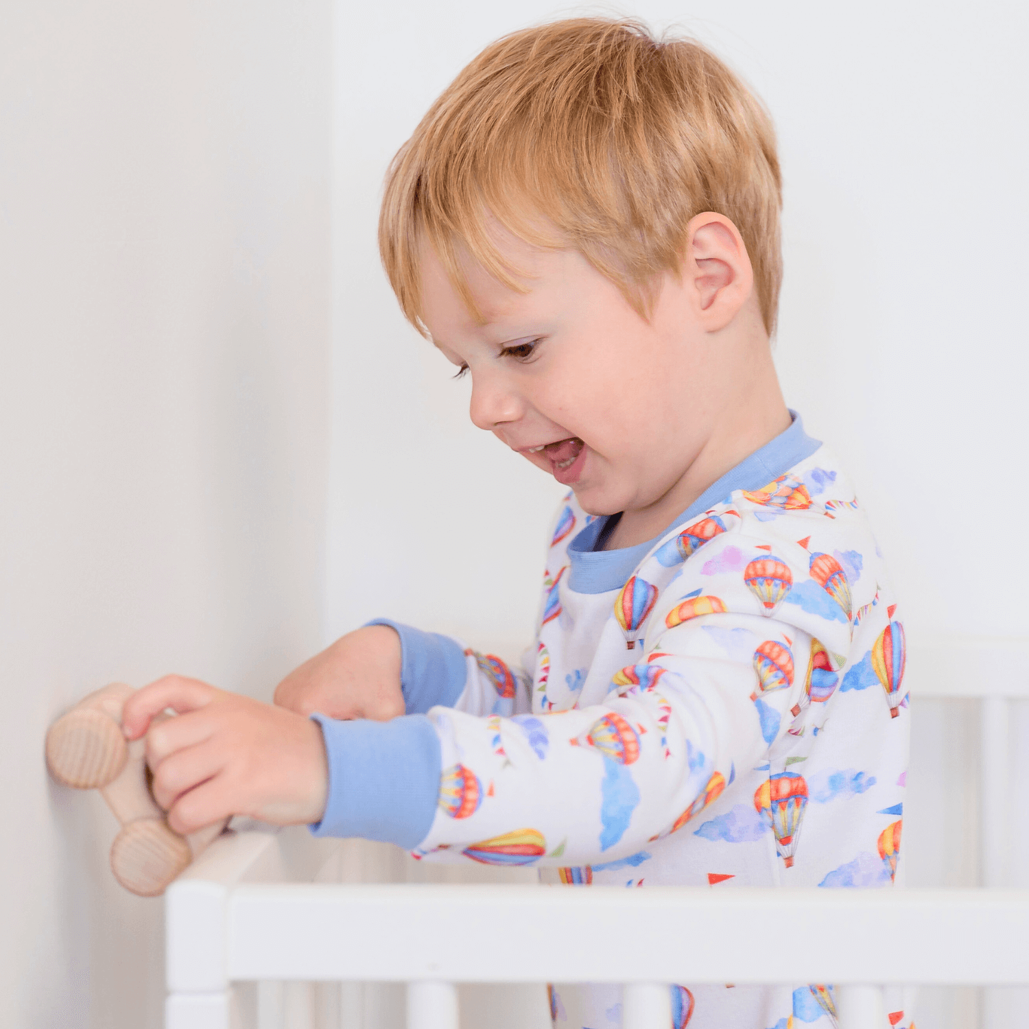 Toddler stood playing in the cot wearing the Up, Up & Away Pyjamas with hot air balloon print made from bamboo and organic cotton from GrowGrows