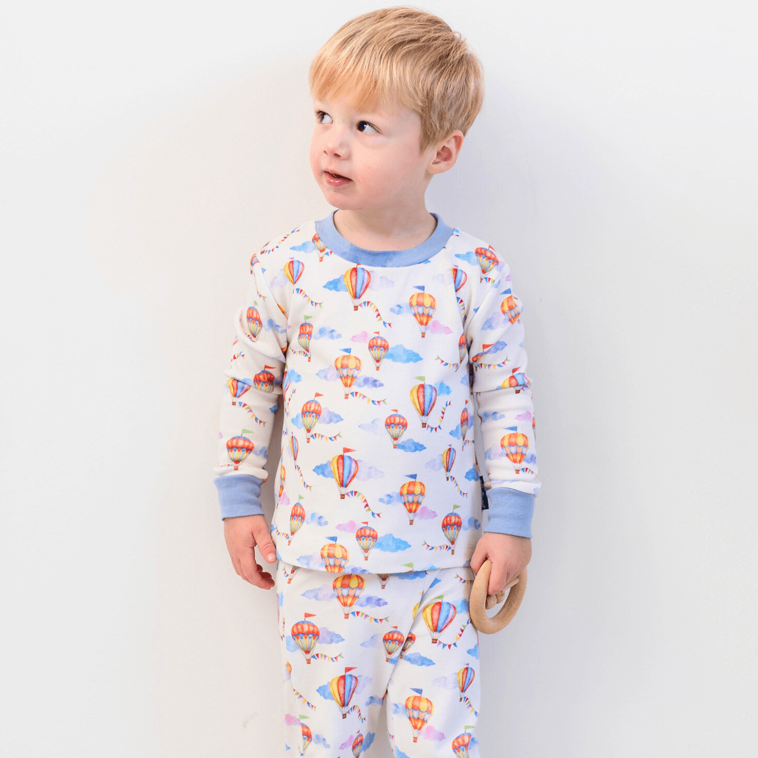 Boy stood against a white wall wearing the Up, Up & Away Pyjamas with hot air balloon print made from bamboo and organic cotton from GrowGrows