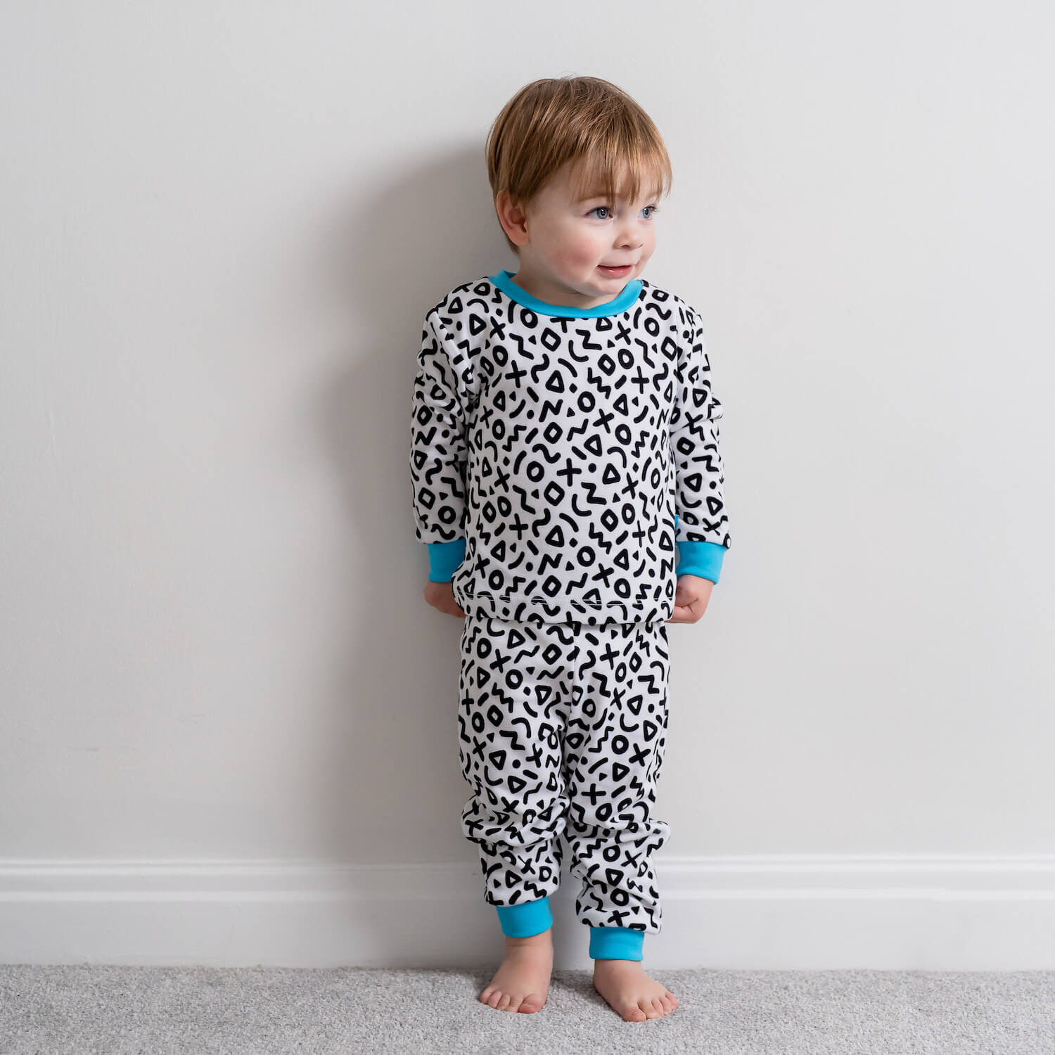 Boy stood against a white background wearing the Delightful Doodle Pyjamas with black and white doodle print and blue trim made from bamboo and organic cotton from GrowGrows