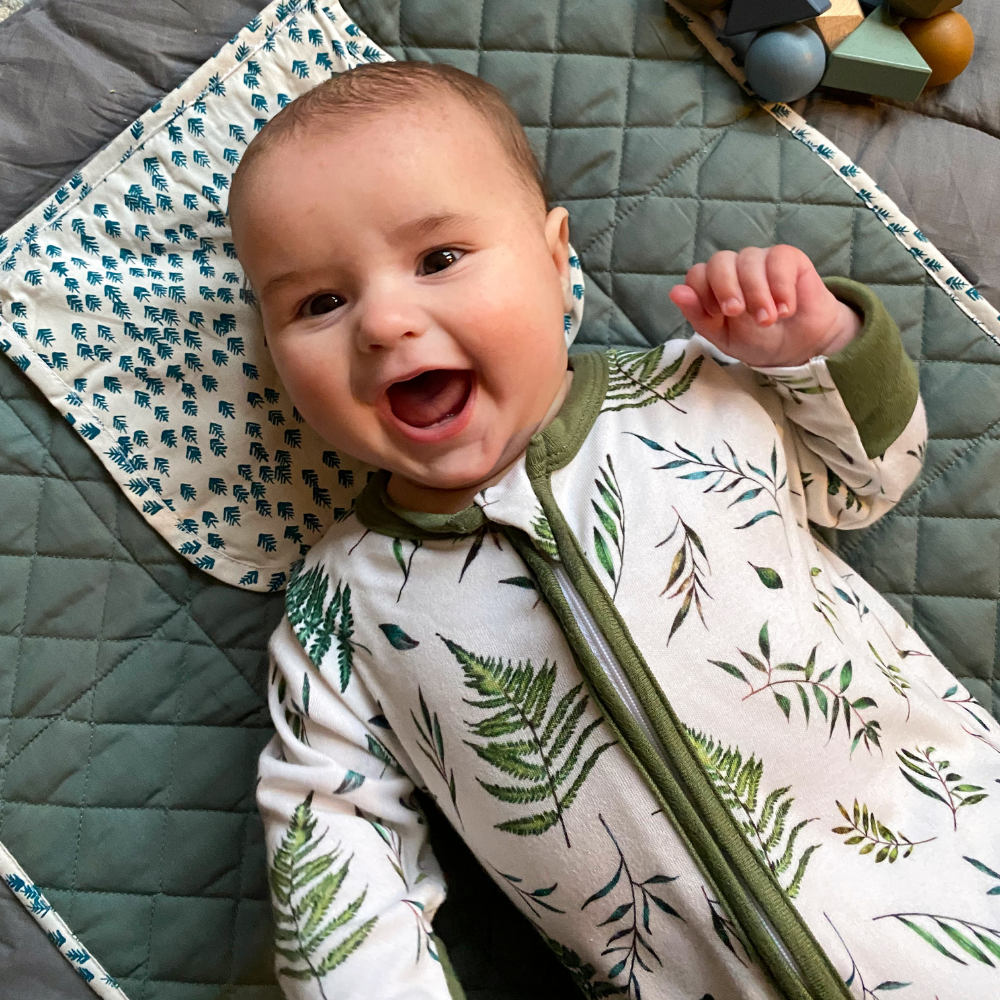 A baby smiling wearing the Country Leaf Sleepsuit with leaf print made from bamboo and organic cotton from GrowGrows