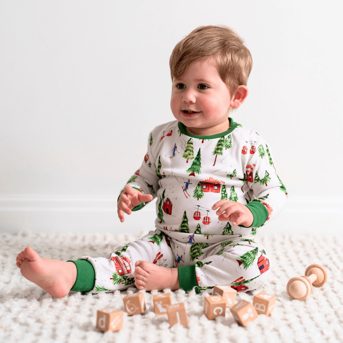 Boy sat playing on the floor wearing the Alpine Adventures Pyjamas with chalet, fir tree and skier print and forest green trim made from bamboo and organic cotton from GrowGrows