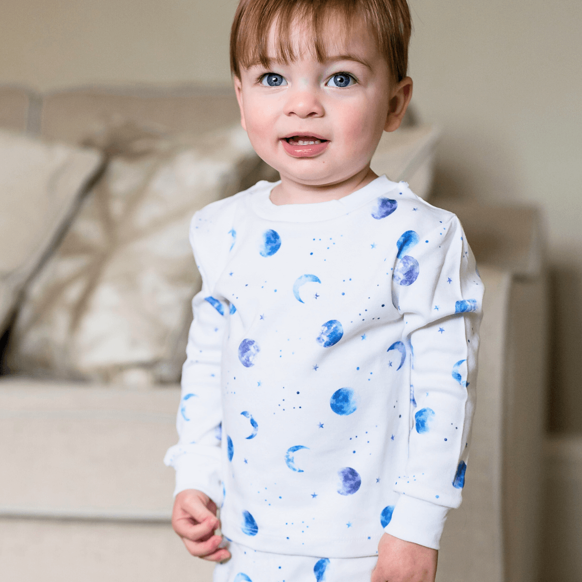Child stood in the living room wearing the Marvellous Moons Pyjamas with blue moon, planet and constellation print made from bamboo and organic cotton from GrowGrows