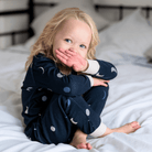 Child sitting on a bed wearing the Midnight Moons Pyjamas with navy moon phase print made from bamboo and organic cotton from GrowGrows