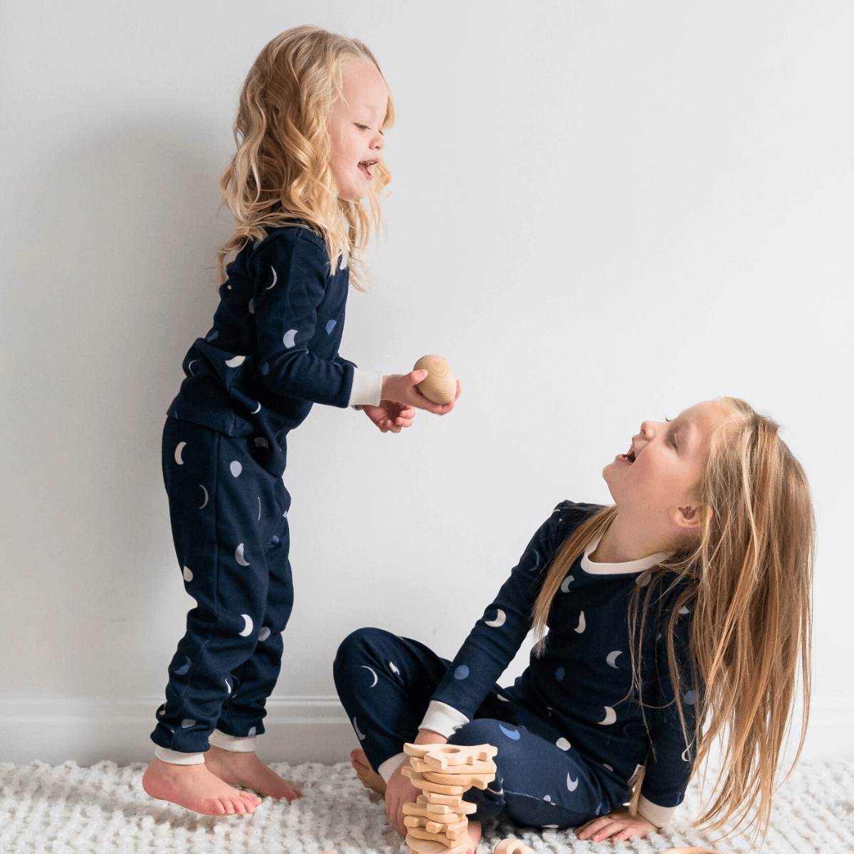 Two children playing wearing matching Midnight Moons Pyjamas with navy moon phase print made from bamboo and organic cotton from GrowGrows