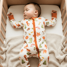 Baby lying asleep in the cot wearing the Autumnal Amazes Sleepsuit with pumpkin and autumn print made from bamboo and organic cotton from GrowGrows