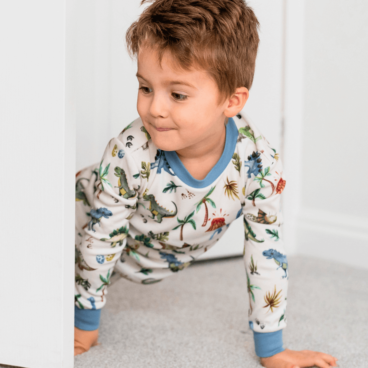 Child peeking around the door wearing the Dandy Dinos Pyjamas with dinosaur print made from bamboo and organic cotton from GrowGrows