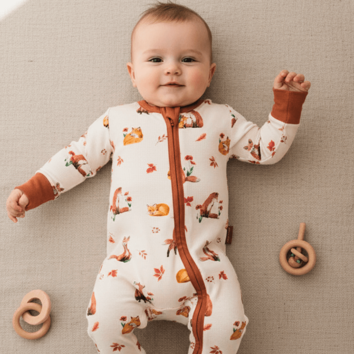 Smiling baby lying on linen blanket wearing the Fluffy Foxes Sleepsuit with fox family print made from bamboo and organic cotton from GrowGrows