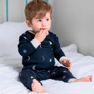 Toddler sat in bed wearing the Midnight Moons Pyjamas with navy moon phase print made from bamboo and organic cotton from GrowGrows