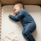 Baby lying in a cot wearing the Navy Ribbed Sleepsuit made from bamboo and organic cotton from GrowGrows