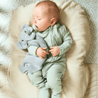 Baby asleep wearing the Sage Ribbed Sleepsuit made from bamboo and organic cotton from GrowGrows and holding the GrowGrows Elephant Comforter