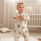 Baby standing in a nursery wearing the Sleepy Sloth Sleepsuit with sloth print made from bamboo and organic cotton from GrowGrows