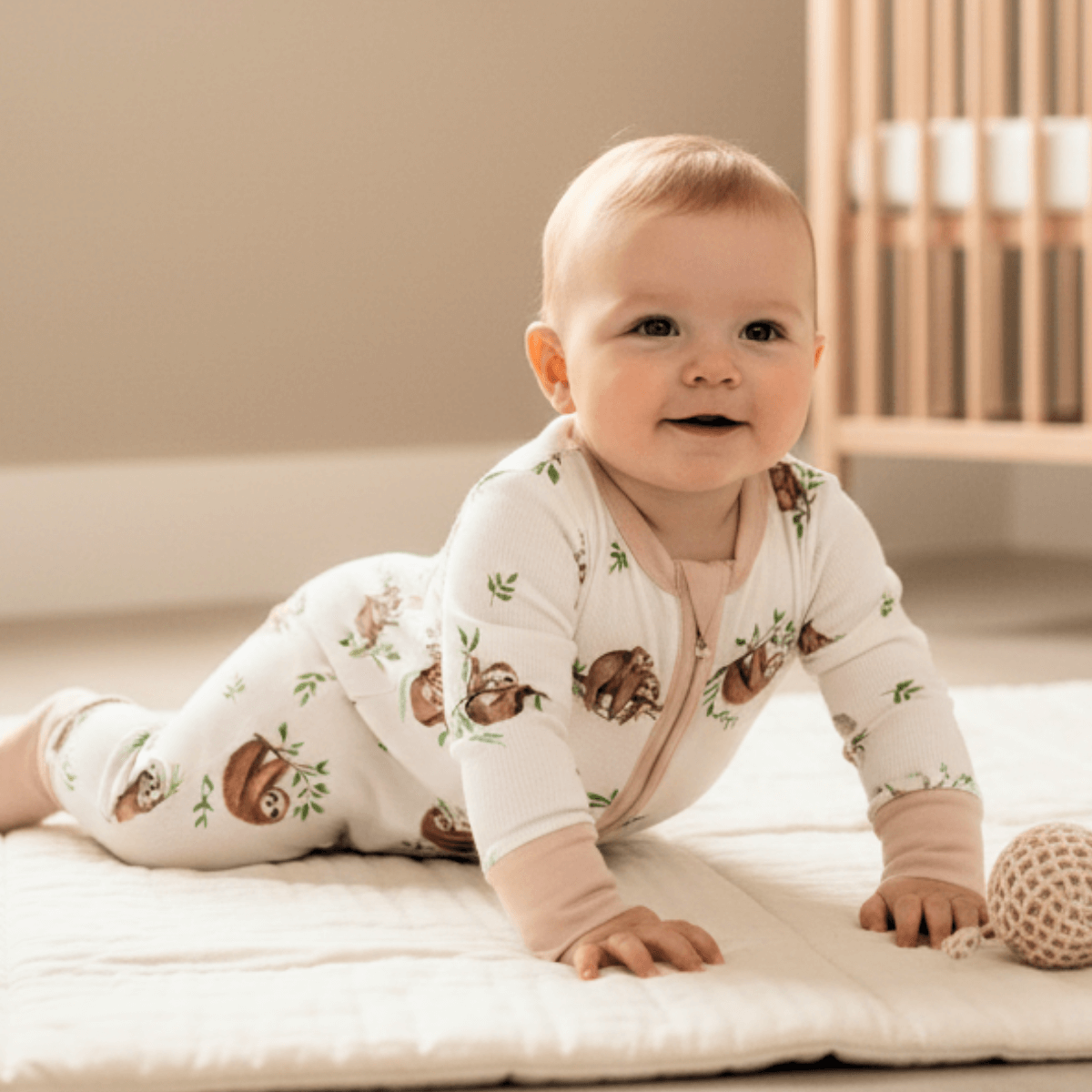 Baby crawling in the nursery wearing the Sleepy Sloth Sleepsuit with sloth print made from bamboo and organic cotton from GrowGrows