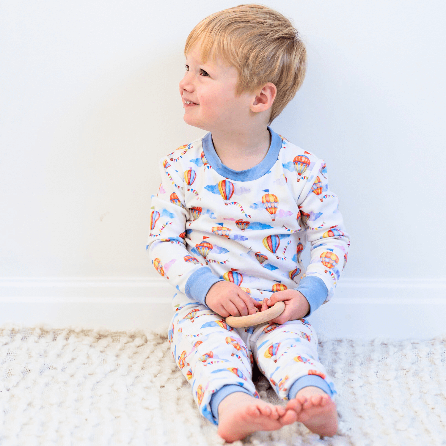 A child sitting on the floor wearing the Up, Up & Away Pyjamas with hot air balloon print made from bamboo and organic cotton from GrowGrows